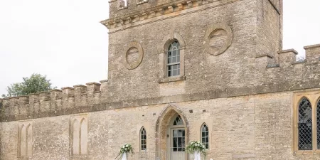 A photograph of the facade of Ivy Lodge in Cirencester with modern and elegant lengths of white chiffon draped up the steps to the ceremony room.