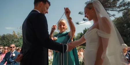 The groom's mother places a cord over the couples hands in a handfasting ritual.