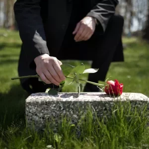 A man placing a red rose on a cremation headstone