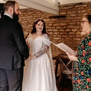 An alternative bride and groom holding hands while Sam White Celebrant officiates their wedding ceremony. The bride is heavily tattooed and the groom has a beard.